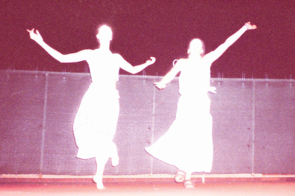 Zdjęcie w odcieniach magenty przedstawia dwie postacie w jasnych, zwiewnych strojach, zastygłe w dynamicznych pozach tanecznych na scenie.