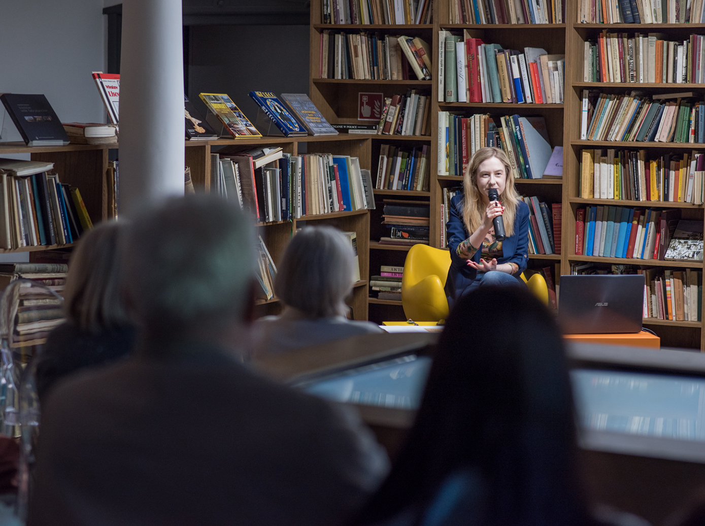 spotkanie w ksiegarni. w środku siedzi młoda kobieta z mikrofonem