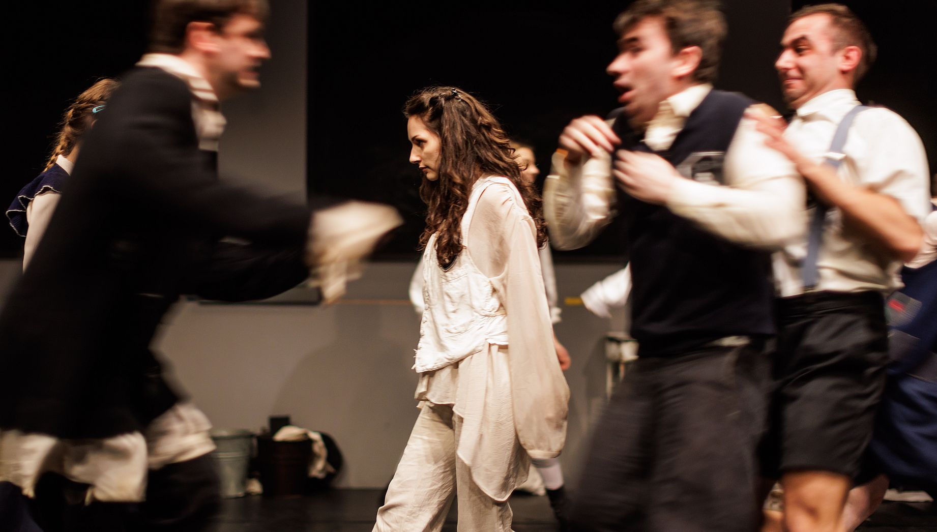 scena w teatrze, aktorzy w dynamicznych pozach, w środku kobieta ubrana na biało, prawdopodobnie scena w szkole