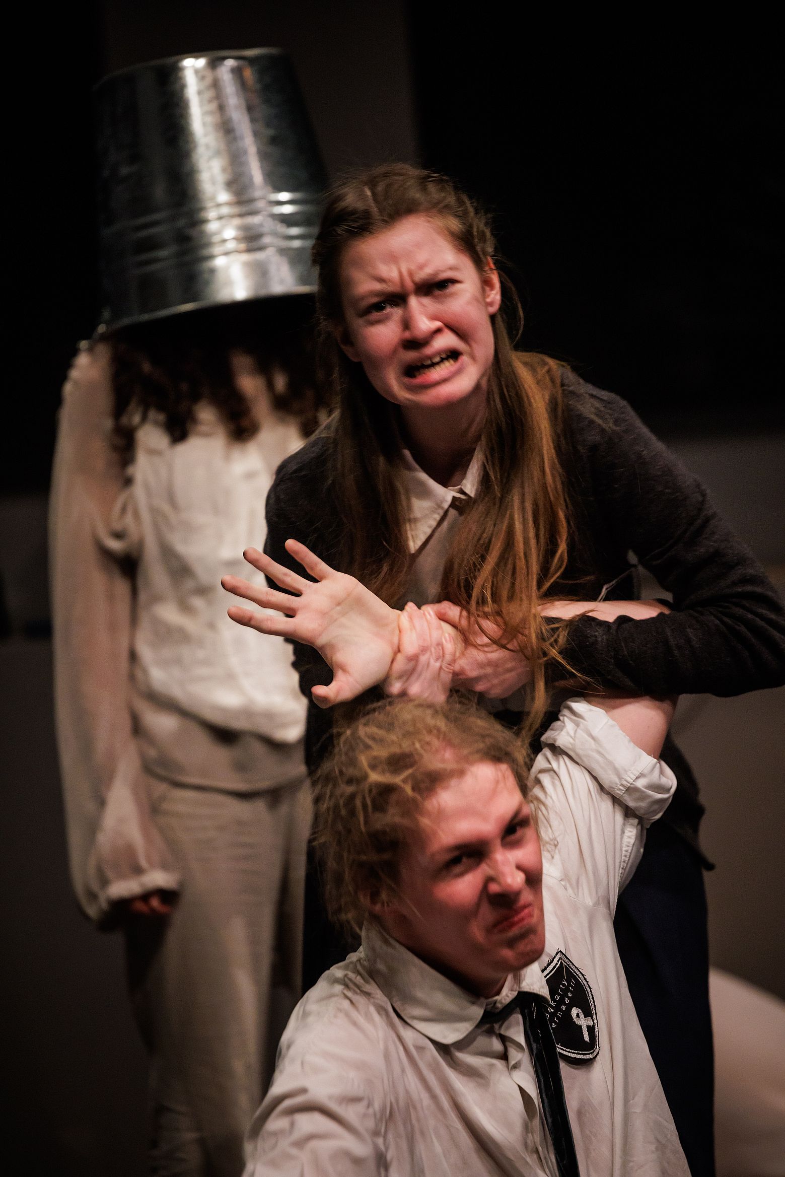 scena w teatrze, dwója aktorów w dramatycznej scenie, w tle jeden ma wiadro na głowie, scena w szkole, 