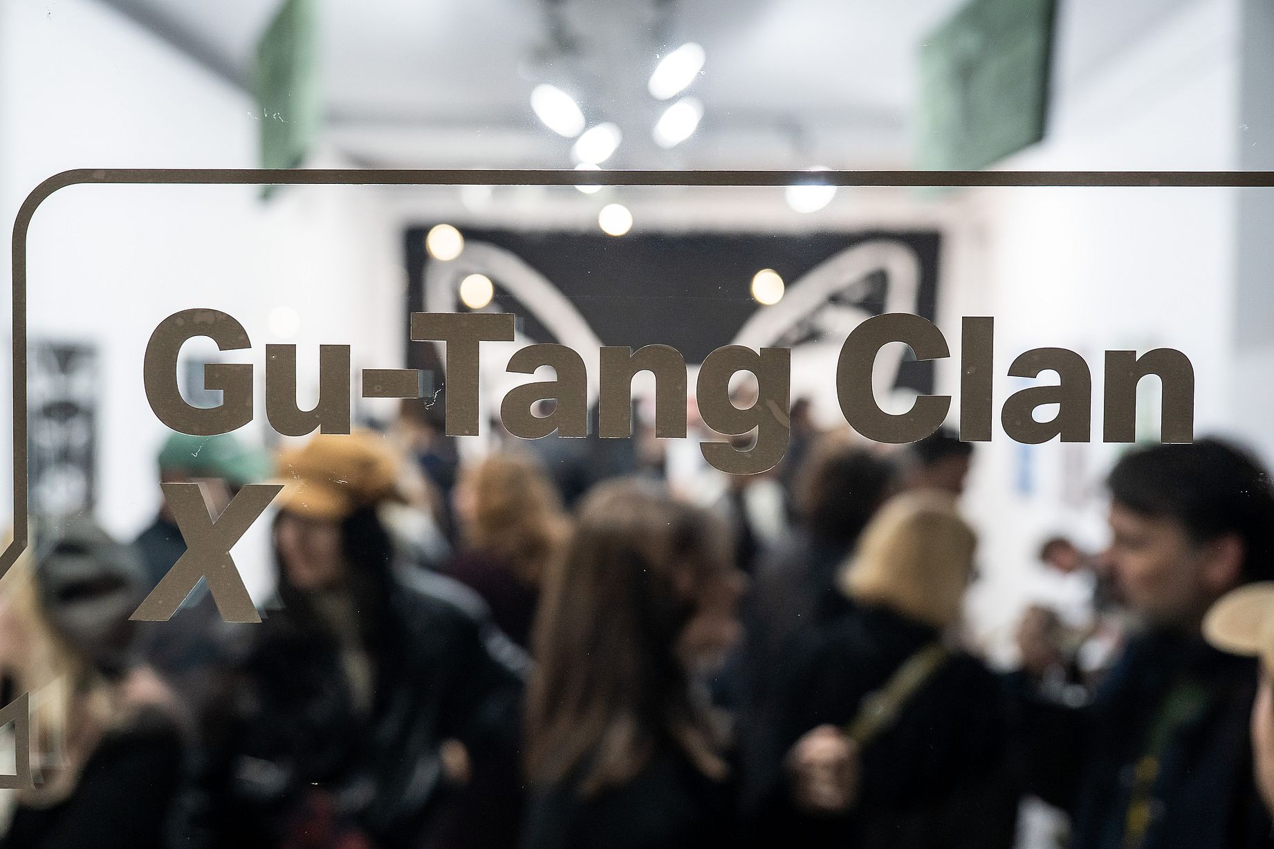Napis Gu tan Clan na szybie w galerii, w tle dużo osób, rozmyty kadr