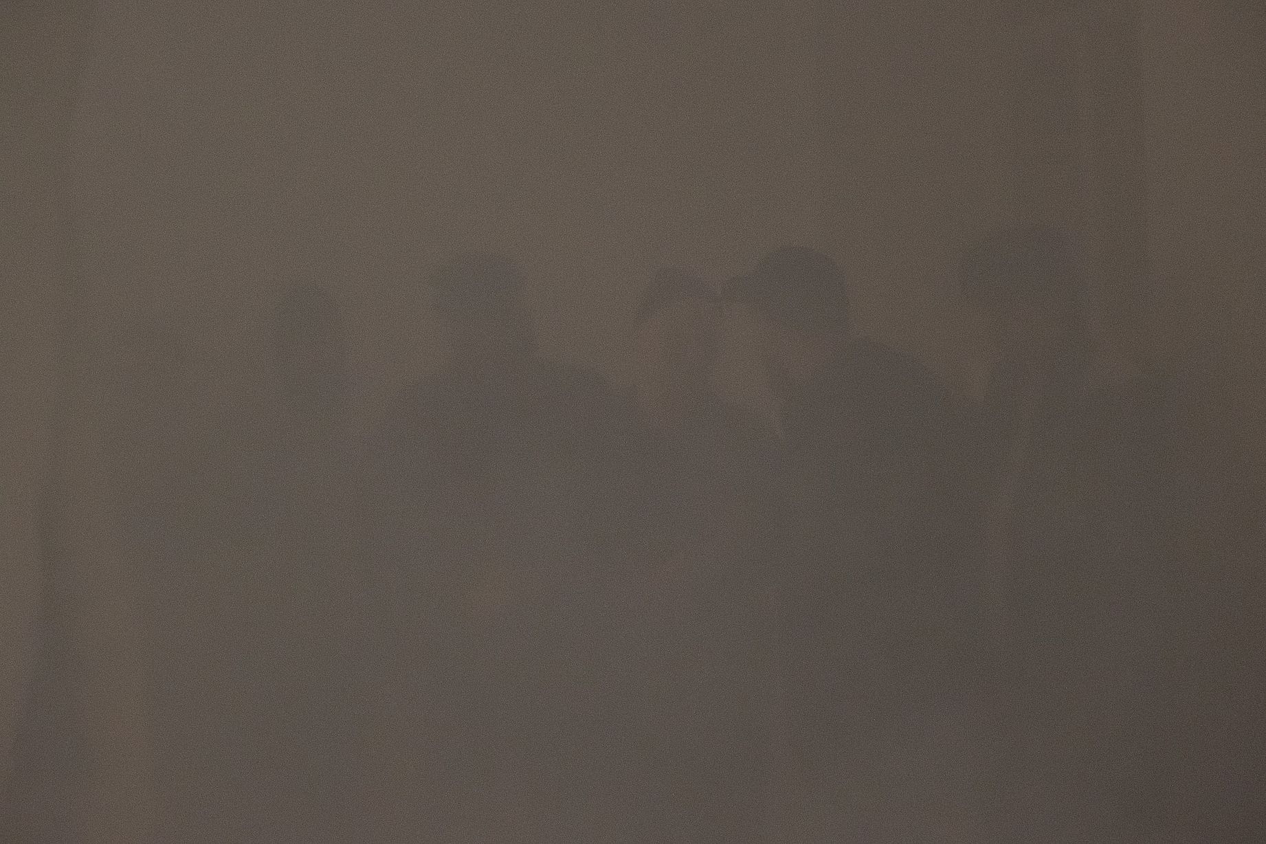 Na niewyraźnym, słabo oświetlonym zdjęciu widoczne są zarysy kilku osób stojących obok siebie w zamglonym lub zadymionym pomieszczeniu. 