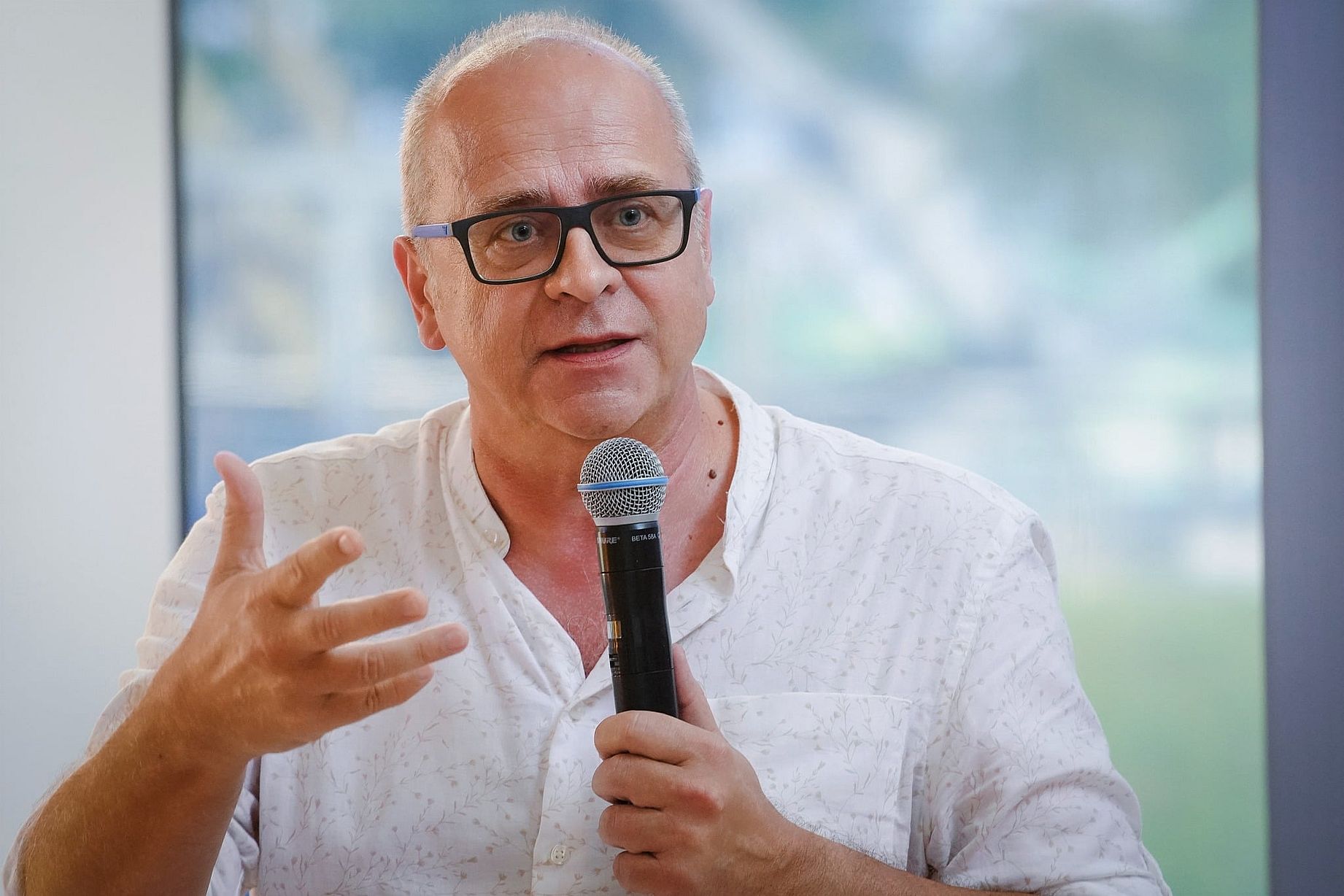 Widoczny na zdjęciu mężczyzna to Jerzy Jarniewicz, polski poeta, krytyk literacki, tłumacz i eseista, profesor Uniwersytetu Łódzkiego. Jest laureatem Nagrody Literackiej „Nike” z 2022 roku za tom poezji „Mondo cane”. Opis zdjęcia Osoba: Jerzy Jarniewicz jest łysiejący, ma czarne okulary z niebieskimi zausznikami i ubrany jest w białą koszulę w delikatny wzór.