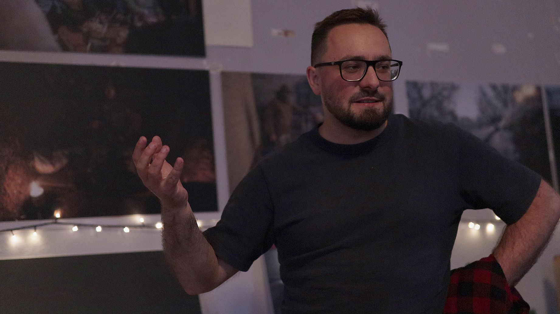 Mężczyzna w okularach, ubrany na czarno, przemawia na spotkaniu, gestykuluje