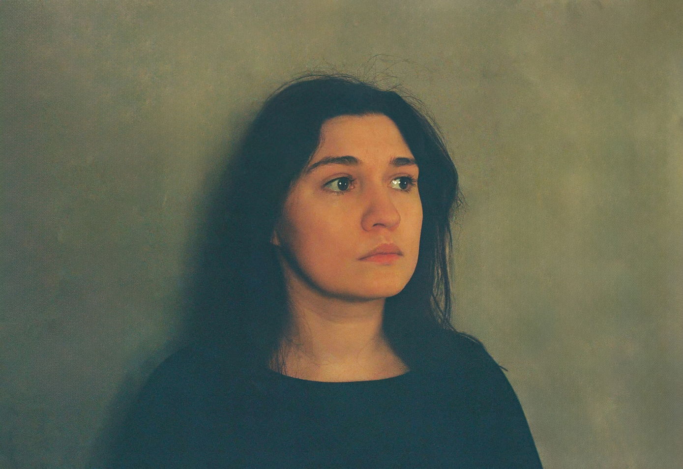 młoda kobieta, dosyć smutna patrzy w lewa stronę, stoi na tle zielonej ściany