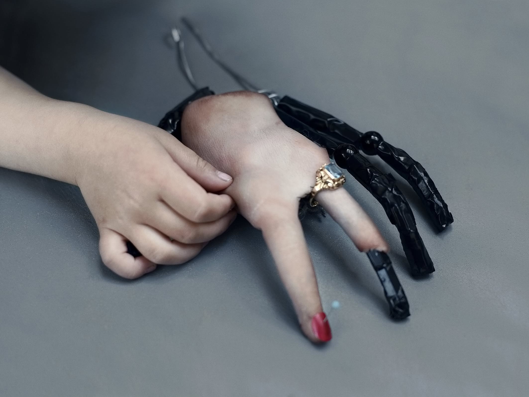 dłoń dzicka przy dłoni hybrydy, jakby człowieka i robota, na ludzkiej dłoni złoty pierścień