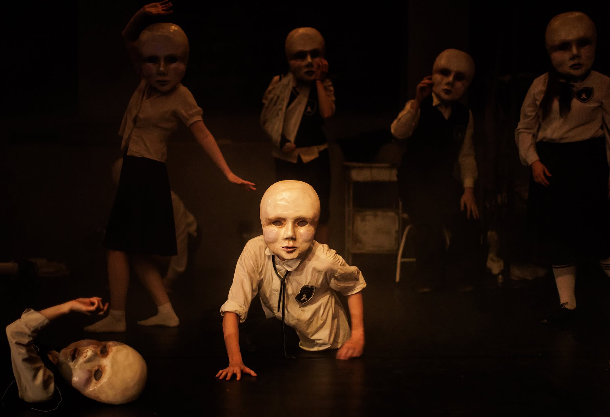 spektakl teatralny, aktorzy w białych maskach, jeden leży, drugi podpiera się dłońmi, czwórka stoi nad nimi