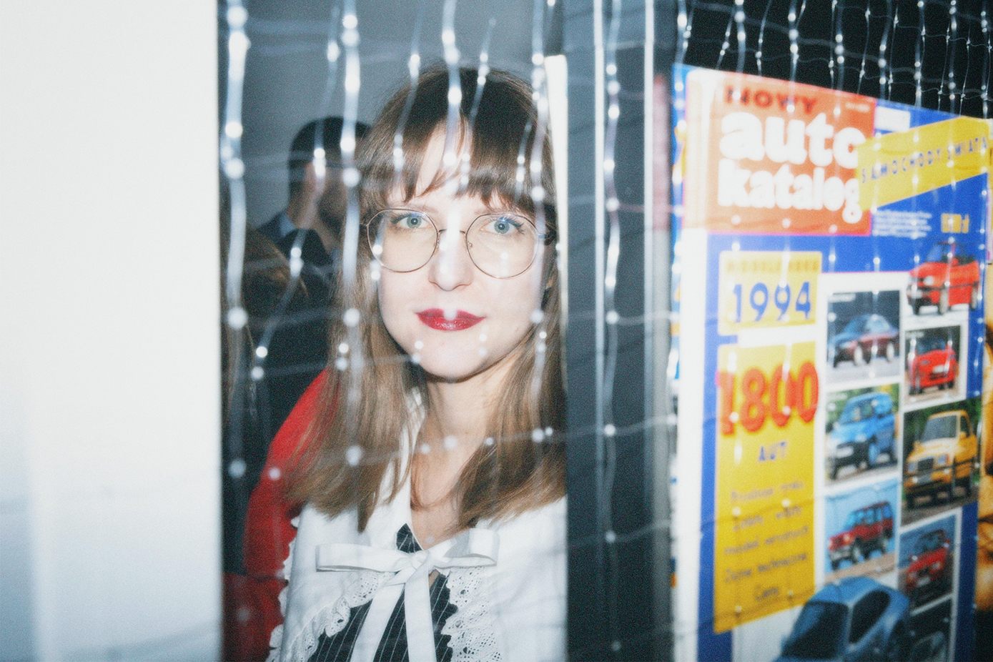 kobieta w okularach, sfotografowana przez szybę, prawdopodobnie w kiosku z gazetamiu