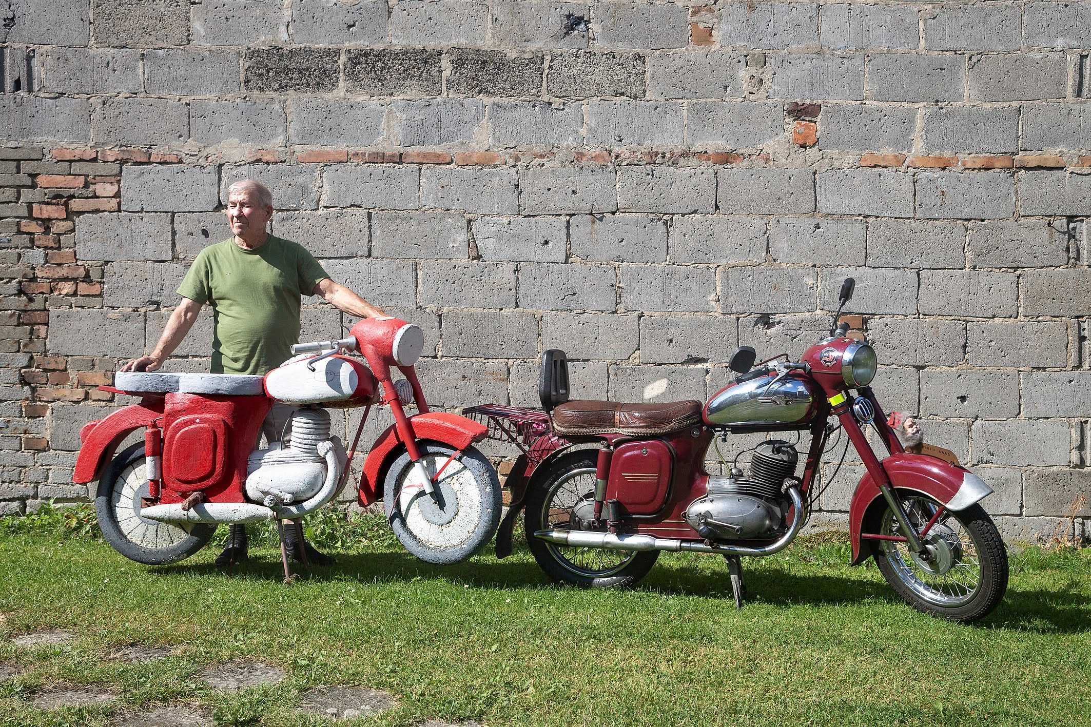 Starszy pan w zionej koszulce stoi przy bordowym motorze Jawa, obok niego model motoru wykonany ze styropianu