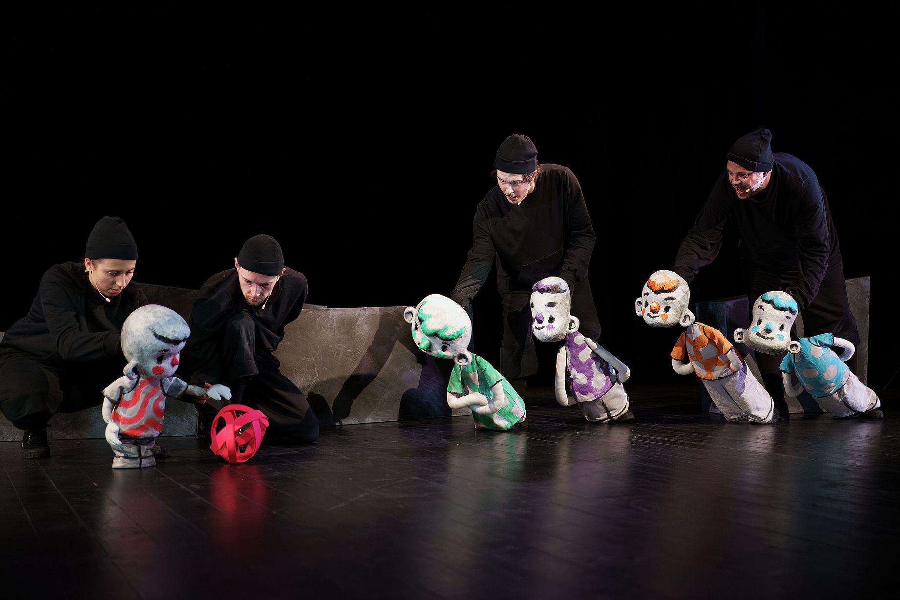 Na scenie w mrocznym oświetleniu czterech ubranych na czarno aktorów animuje kilka lalek chłopców o szarym ciele i czerwonych policzkach, używając czerwonej wstążki