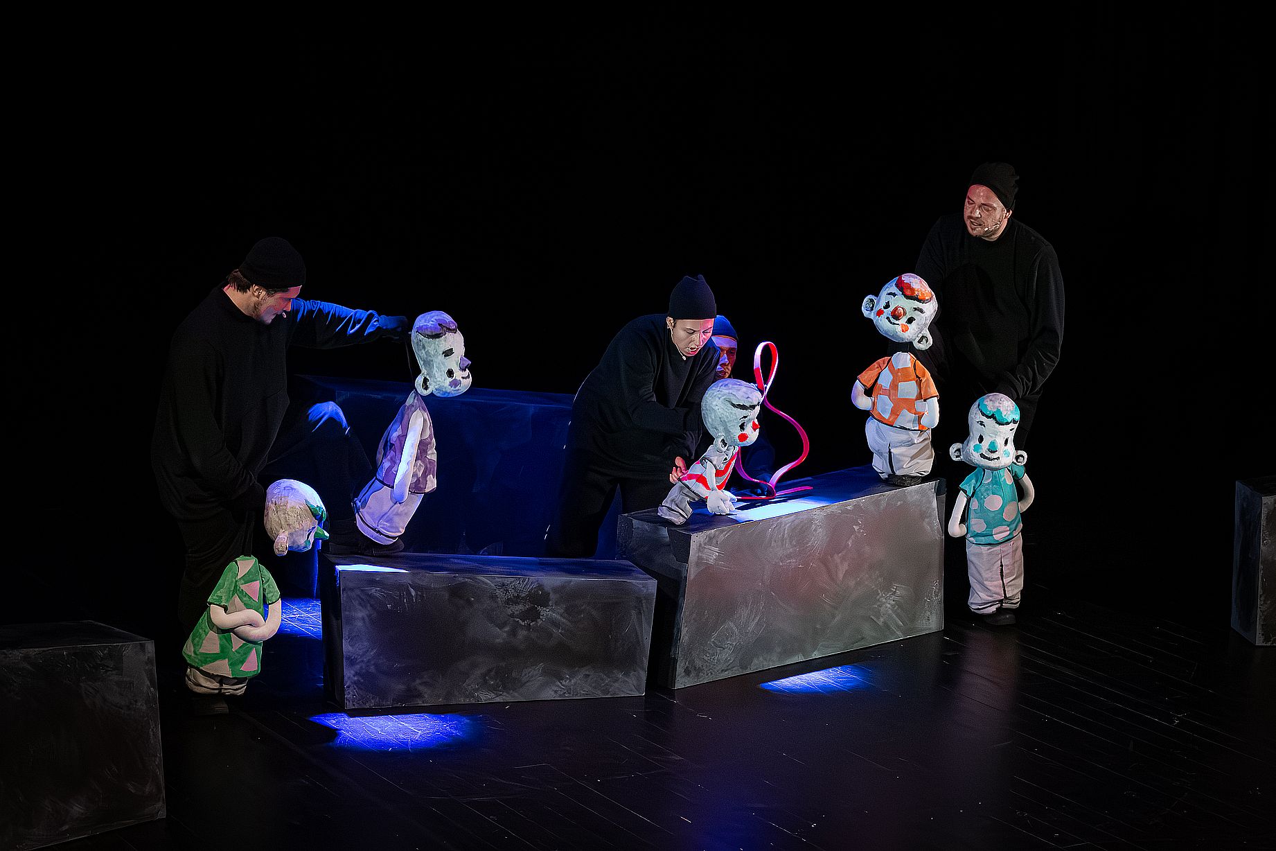 Na scenie w mrocznym oświetleniu czterech ubranych na czarno aktorów animuje kilka lalek chłopców o szarym ciele i czerwonych policzkach, używając czerwonej wstążki